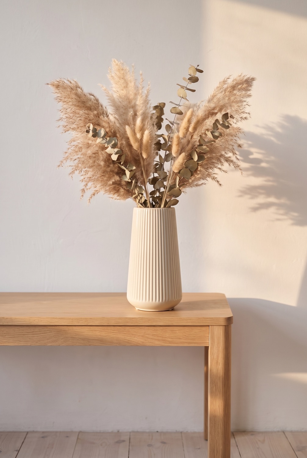 Cream ribbed ceramic vase holding dried pampas and eucalyptus on a light oak table